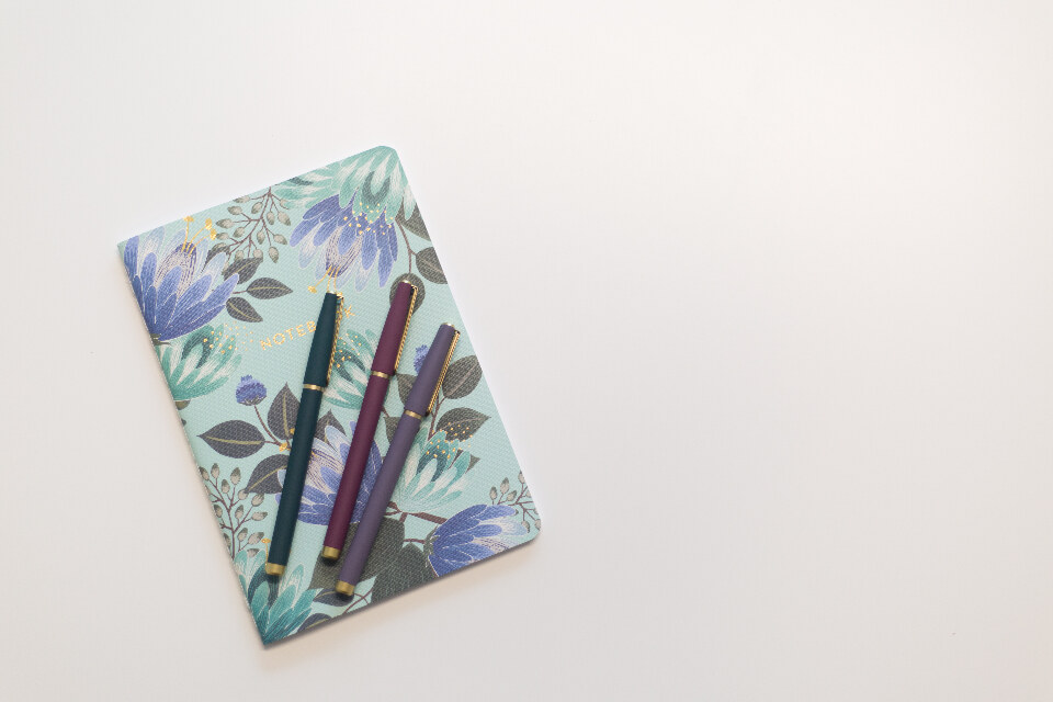 Jegyzetfüzet és tollak egy fehér asztalon a napi tervezéshez